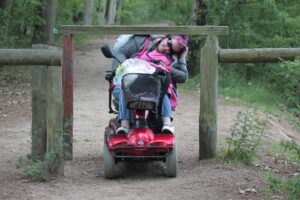 Dame i kørestol forsøger at køre gennem låge, der har en overligger, der er for lav til, at hun kan komme igennem uden problemer.